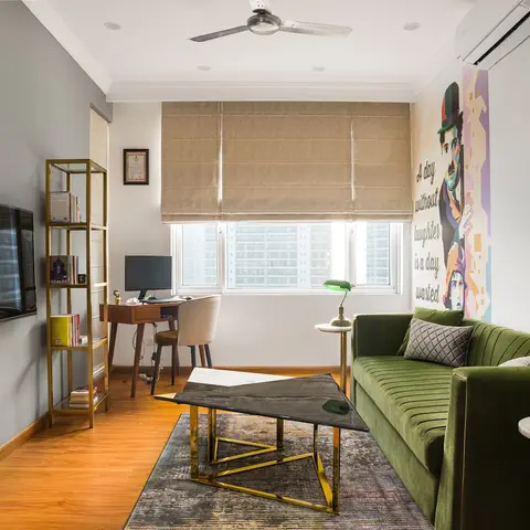 A living room with a channel-tufted emerald velvet sofa, gold-framed ladder shelving