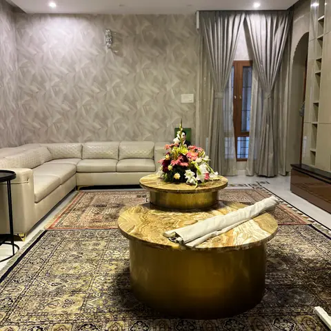 A living room with a cream leather sectional, layered Persian-style rugs, twin round onyx-and-brass coffee tables, silvery silk drapes