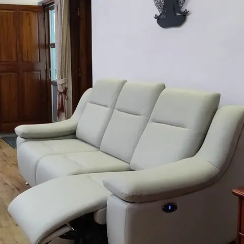 A living room with a cream leather power-reclining sofa, a wood-plank floor, and a metal Buddha silhouette wall art piece.