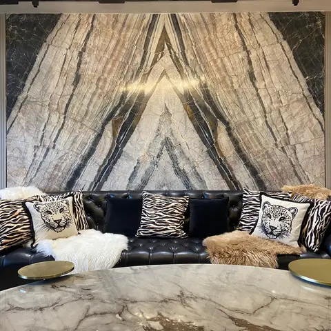 A living room with a dramatic bookmatched marble feature wall behind a black tufted leather sofa styled with zebra and leopard-print cushions and faux-fur