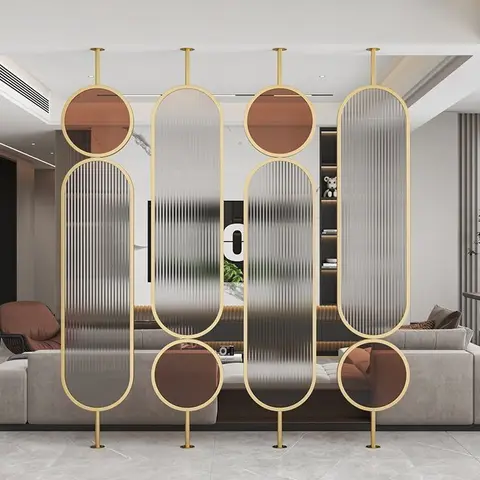 A living room with a floor-to-ceiling brass-ringed fluted-glass partition screen separating the seating area from a dark built-in TV wall unit.