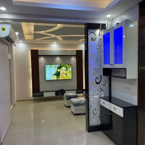 A living room with a fluted-panel TV wall under a geometric POP false ceiling, beside a laser-cut jaali partition unit with blue LED-lit glass display cabinets.