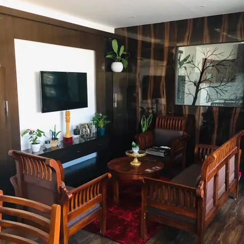 A living room with a glossy dark wood-textured feature wall behind carved wooden slat-back sofas around a red shaggy rug
