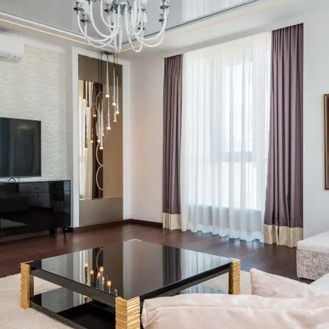 A living room with a glossy stretch ceiling, a cluster pendant chandelier, mauve floor-to-ceiling curtains