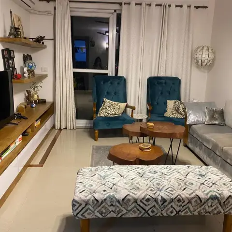 A living room with a grey sectional sofa and two teal tufted armchairs around live-edge wood nesting coffee tables