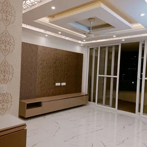 A living room with a laser-cut jaali cornice bordering a layered false ceiling, damask wallpaper on the side wall