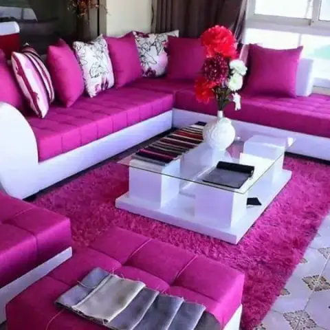 A living room with a magenta L-shaped sectional sofa and matching ottomans on a fuchsia shag rug around a white glass-top coffee table.