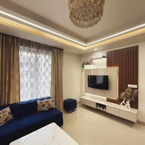 A living room with a navy tufted chesterfield sofa facing a fluted wood-panelled TV wall with backlit marble niche, under a crystal chandelier