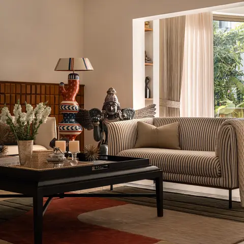 A living room with a striped bolster sofa, a black lacquered coffee table styled with a curated books-and-candles tray
