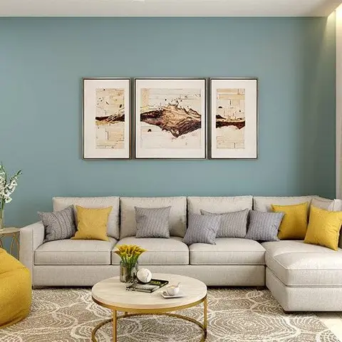 A living room with a teal accent wall behind a light grey sectional sofa styled with mustard and grey cushions, a mustard bean bag
