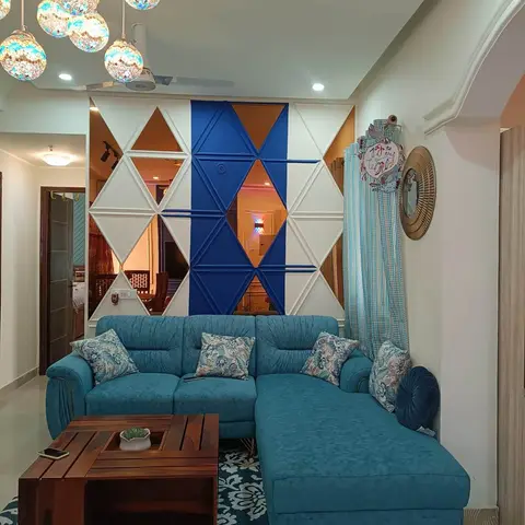 A living room with a teal L-shaped sofa and floral cushions facing a geometric triangular mirror-and-blue accent partition wall