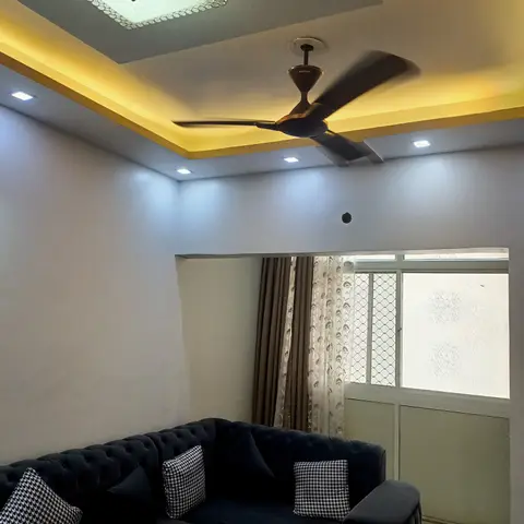 A living room with a tufted navy chesterfield sofa, houndstooth cushions, and a warm LED cove-lit false ceiling with a crystal flush-mount fixture.