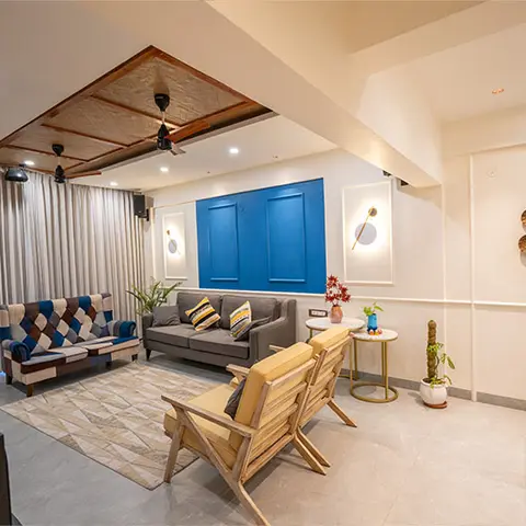 A living room with a wood-slat coffered ceiling over a mixed seating arrangement of a grey sofa, a checkered patchwork sofa, and open wood-frame armchairs
