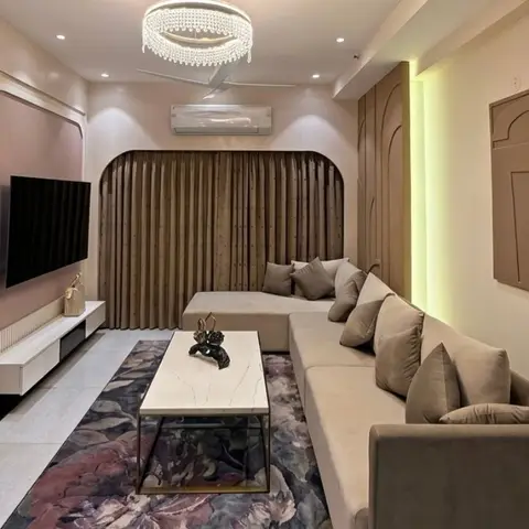 A living room with an arched fluted-curtain alcove behind a taupe sectional sofa, a crystal ring chandelier, a marble-top coffee table on a floral rug