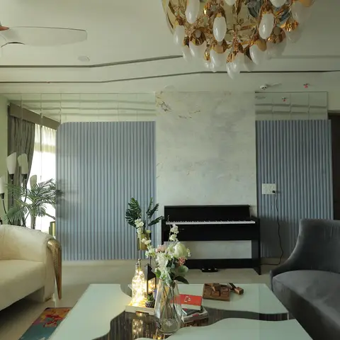 A living room with an upright piano set against a marble feature wall flanked by fluted grey panelling, under an ornate gold-and-glass chandelier.