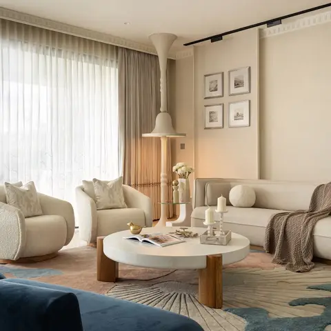 A living room with boucle swivel armchairs and a navy velvet sofa around a round marble-and-wood coffee table, sheer floor-to-ceiling curtains