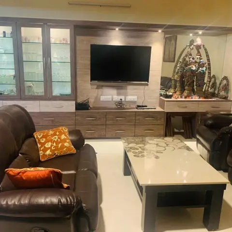 A living room with brown leather sofas and orange floral cushions facing a wood-panel TV unit with a glass-front crockery display cabinet