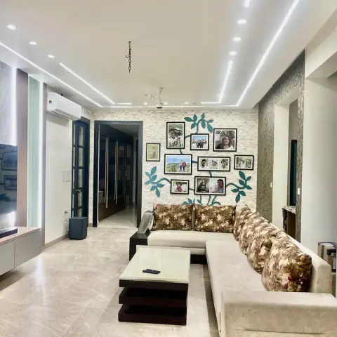 A living room with linear cove-lit ceiling channels, a stone-clad accent wall styled as a photo tree with framed family portraits