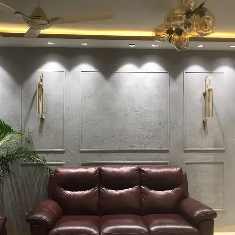 A living room with textured plaster wall panels lit by brass sconces, a cove-lit ceiling, an amber glass cluster chandelier, and a maroon leather sofa.