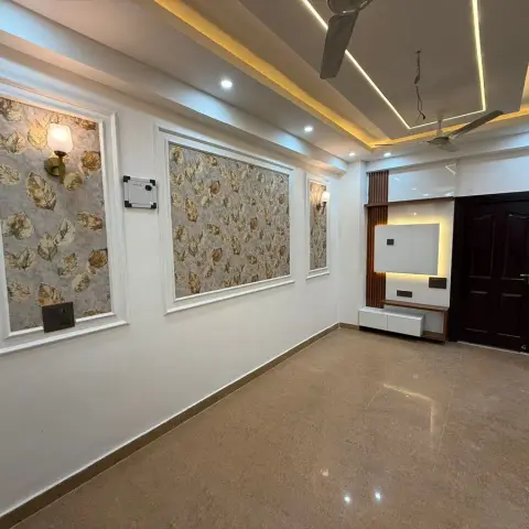 A living room with three leaf-print wallpaper panels framed in white moulding, a multi-tier cove-lit pop ceiling with two fans