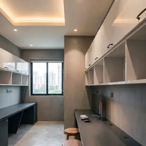 A long built-in study counter with overhead white gloss cabinets and a cove-lit ceiling, paired with wooden stools along a grey stone-effect wall.
