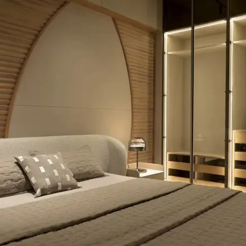 A low bed with a curved boucle headboard set against a fan of curved oak slats radiating from an upholstered centre panel