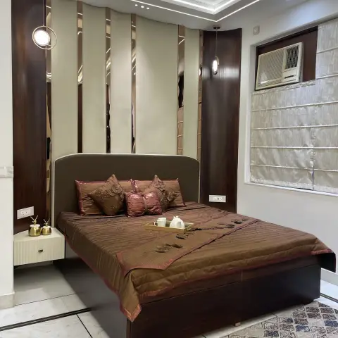 A luxury bedroom with a dark wood and mirrored-strip panelled headboard wall, a geometric LED cove ceiling, bronze bedding with a styled welcome tray