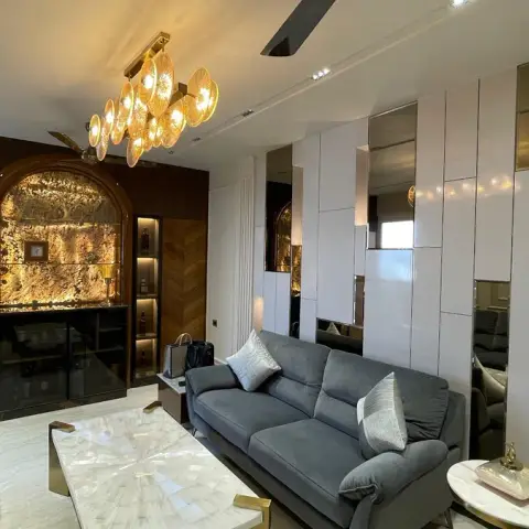 A luxury living room with a backlit onyx bar nook framed by a wooden arch, brass-mirrored wall panelling