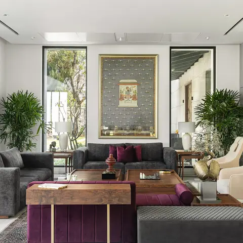 A luxury living room with charcoal grey sofas and a burgundy velvet channel-tufted daybed with brass trim around a walnut coffee table