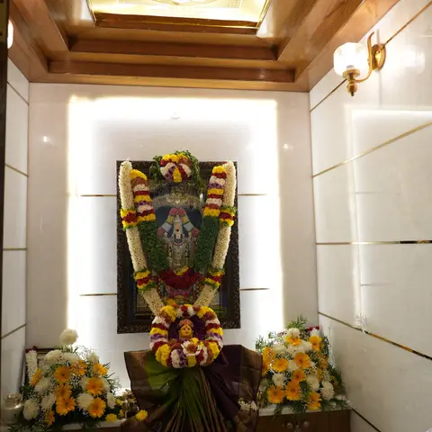 A marble-clad pooja alcove with a backlit gold Sri Yantra ceiling panel, wood ceiling trim, and a mandir framed by garlands and festive flowers