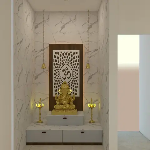 A marble-clad pooja niche with a backlit wooden Om jaali panel, a gold Ganesh idol, hanging brass bells and a two-drawer storage unit below.