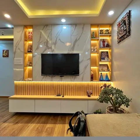 A marble-clad TV feature wall with backlit fluted panelling and side display niches holding curios, framed by a wood floor and a potted jade plant.