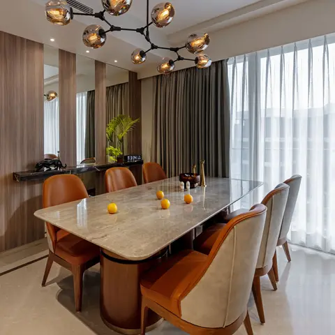 A marble-top dining table on a brass-ringed wood plinth surrounded by eight tan and grey leather chairs