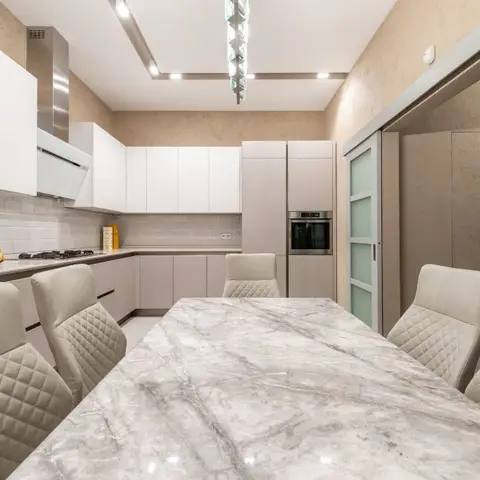 A marble-top dining table with quilted cream leather chairs beneath a vertical crystal pendant light