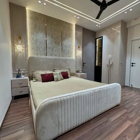A master bedroom with a channel-tufted cream velvet bed against a gold-trimmed textured wallpaper panel
