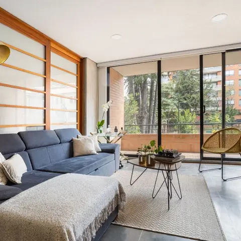 A mid-century living room with a navy sectional sofa, a brass arc floor lamp and a wood-slat sliding partition beside floor-to-ceiling glass doors to a balcony.