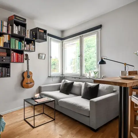A modular cube bookshelf and a guitar hung on the wall sit beside a grey sofa and a black metal-frame coffee table on a wood floor.