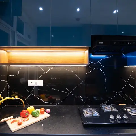 A modular kitchen with glossy teal overhead cabinets, a black-and-white veined marble backsplash and countertop