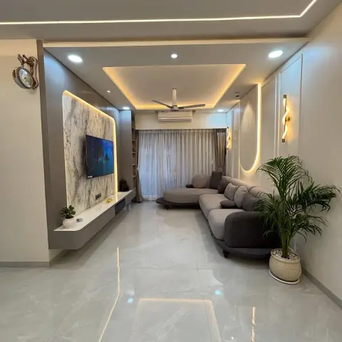 A narrow living room with a backlit book-matched marble TV feature wall, a cove-lit stepped false ceiling