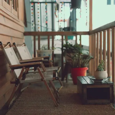 A narrow wood-slatted balcony with two folded canvas camp chairs, a terracotta potted plant, and a wooden crate used as a side table for a succulent.