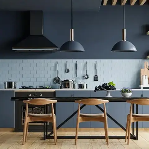 A navy-blue kitchen with a light-blue subway-tile backsplash and black dome pendant lights hanging over an island lined with wooden dining chairs.