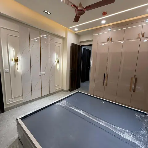A newly finished bedroom with a beige high-gloss wardrobe wall, a white marble-panel accent wall with brass wall sconces