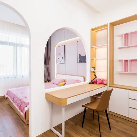 A pink-and-white kids' room with an arched bed alcove lit by cove lighting, a built-in study desk with pink open shelving, and grey curtains at the window.