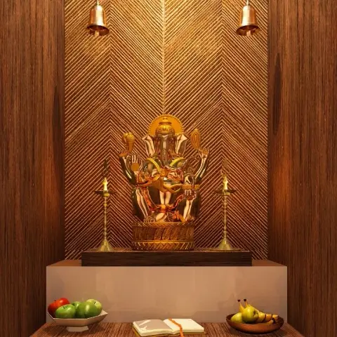 A pooja niche with a herringbone-textured gold wall panel behind a brass Ganesha idol, hanging temple bells