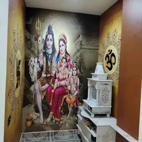 A pooja niche with a large mural of Shiva's family on the back wall, Om medallion decals on the side walls, and a white marble mandir unit with jaali fretwork
