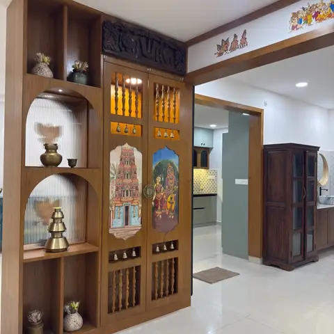 A pooja unit with a carved wood pediment, hand-painted temple and deity motifs on the cabinet doors, brass bells