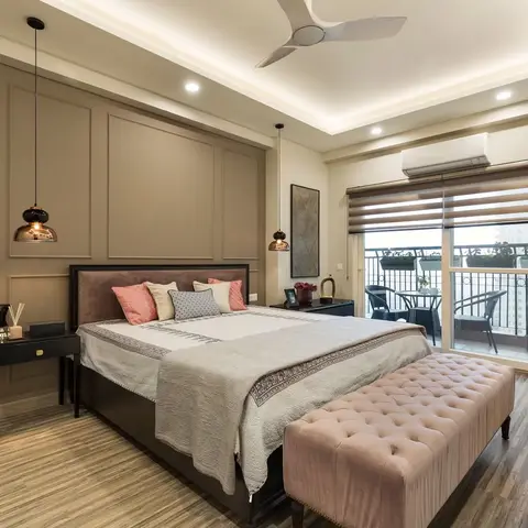A primary bedroom with a taupe moulded panel headboard wall, twin copper pendant lights, a blush tufted bench at the foot of the bed