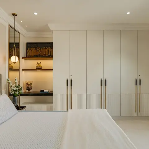 A primary bedroom with a tufted grey leather headboard, a full-height six-door wardrobe with brass pulls and a fluted base