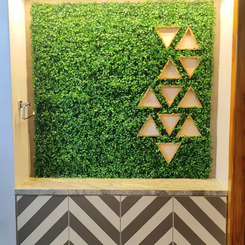 A real photo, entrance nook with an artificial green wall inset with triangular wood display shelves above a chevron-patterned shoe cabinet with marble top.