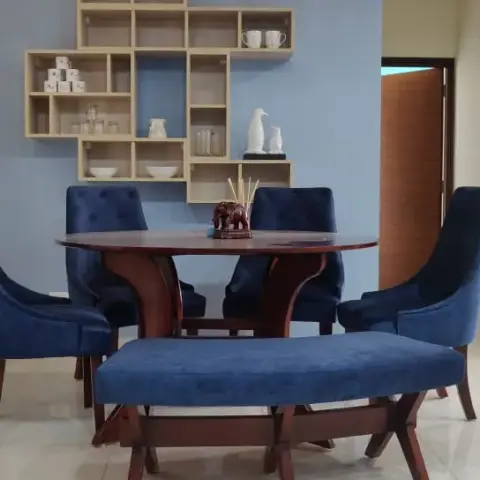 A round polished-wood dining table with navy velvet tub chairs and a matching navy bench